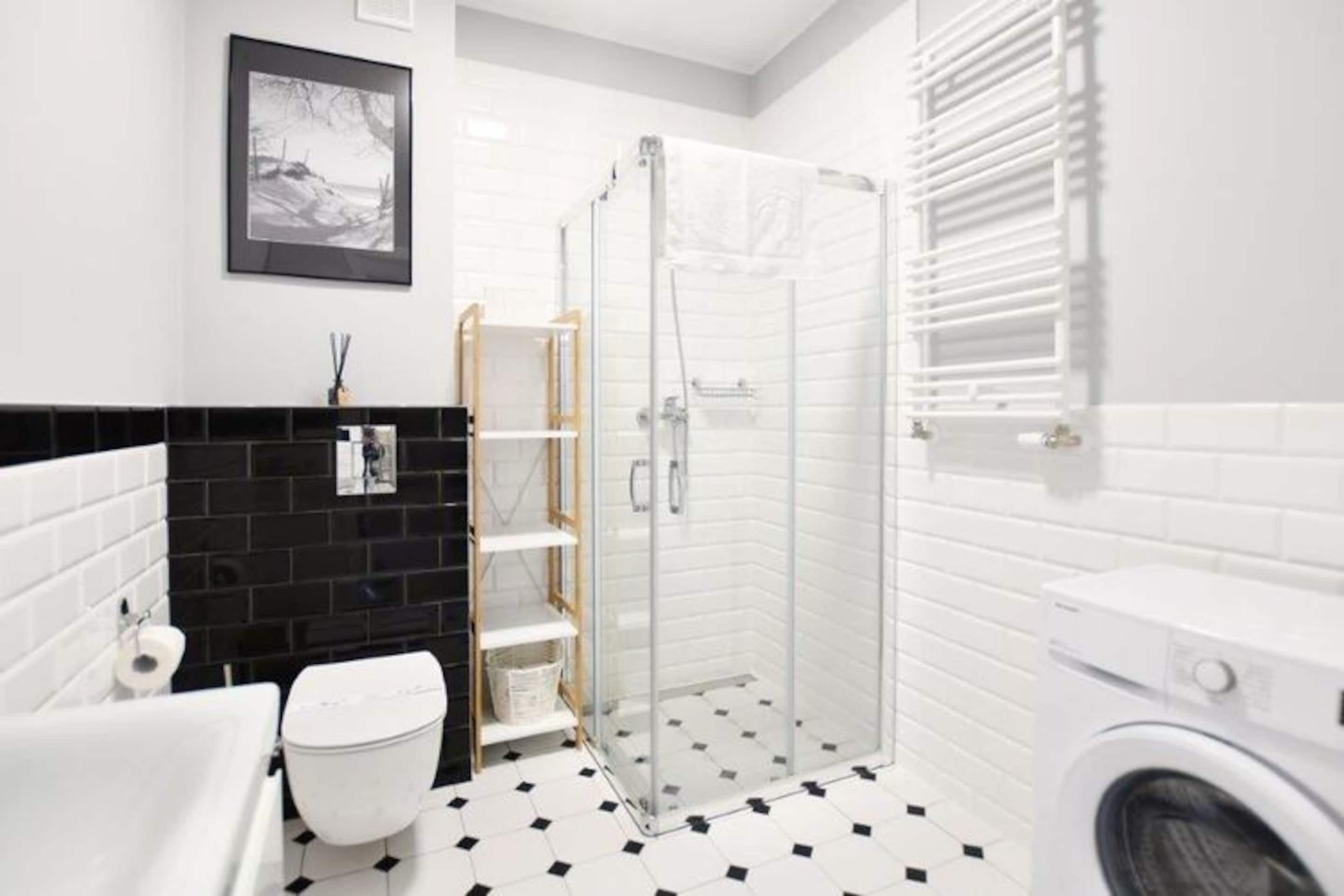 Une salle de bain moderne avec une douche à parois de verre, des toilettes blanches, un carrelage noir et blanc et un lave-linge blanc.
