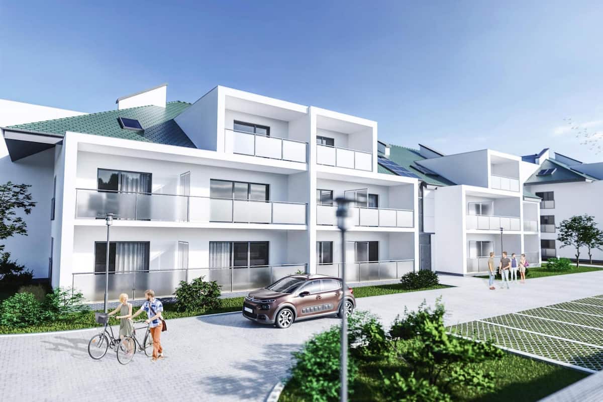 A modern multi-story residential building with balconies, a paved driveway, and a car parked in front.