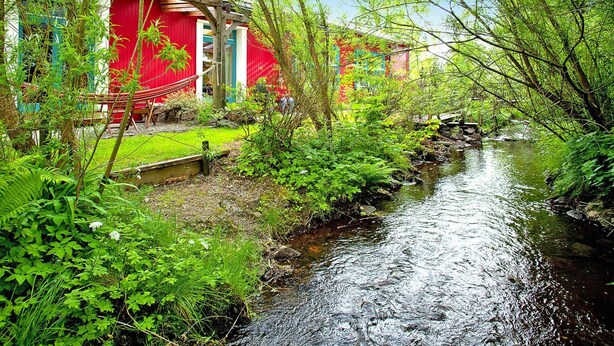 Un jardín tranquilo con un pequeño arroyo, un edificio rojo y una hamaca.