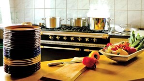 Una cocina con estufa, ollas, tabla de cortar, cuchillo y un bol de verduras.