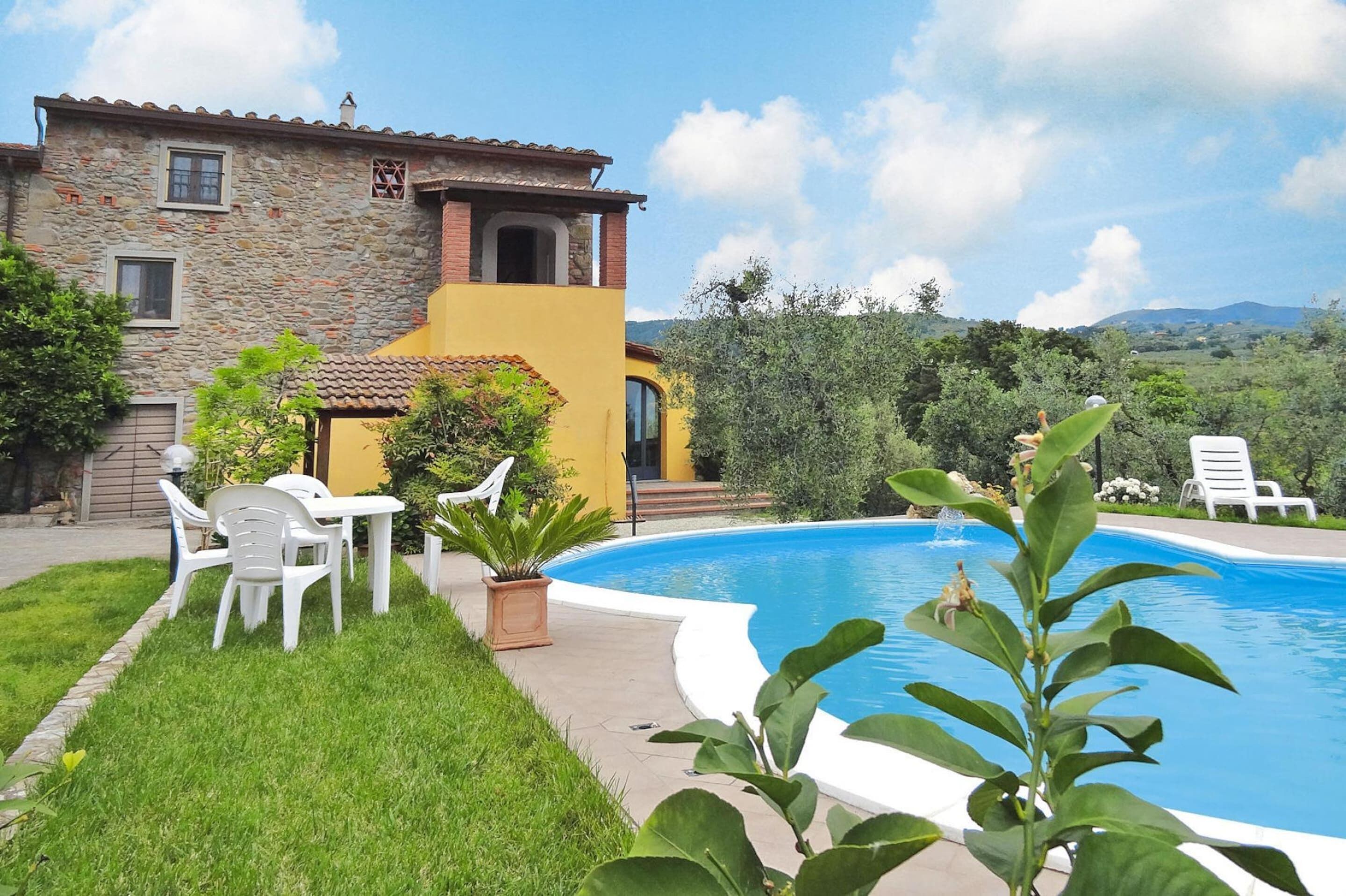 A stone building with a yellow facade, a swimming pool, and outdoor seating.
