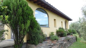 Un bâtiment jaune avec un mur de soutènement en pierre, une grande fenêtre et diverses plantes.