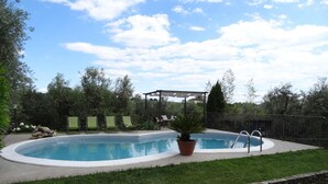 Une piscine bordée de pierres, une pergola et trois chaises longues.