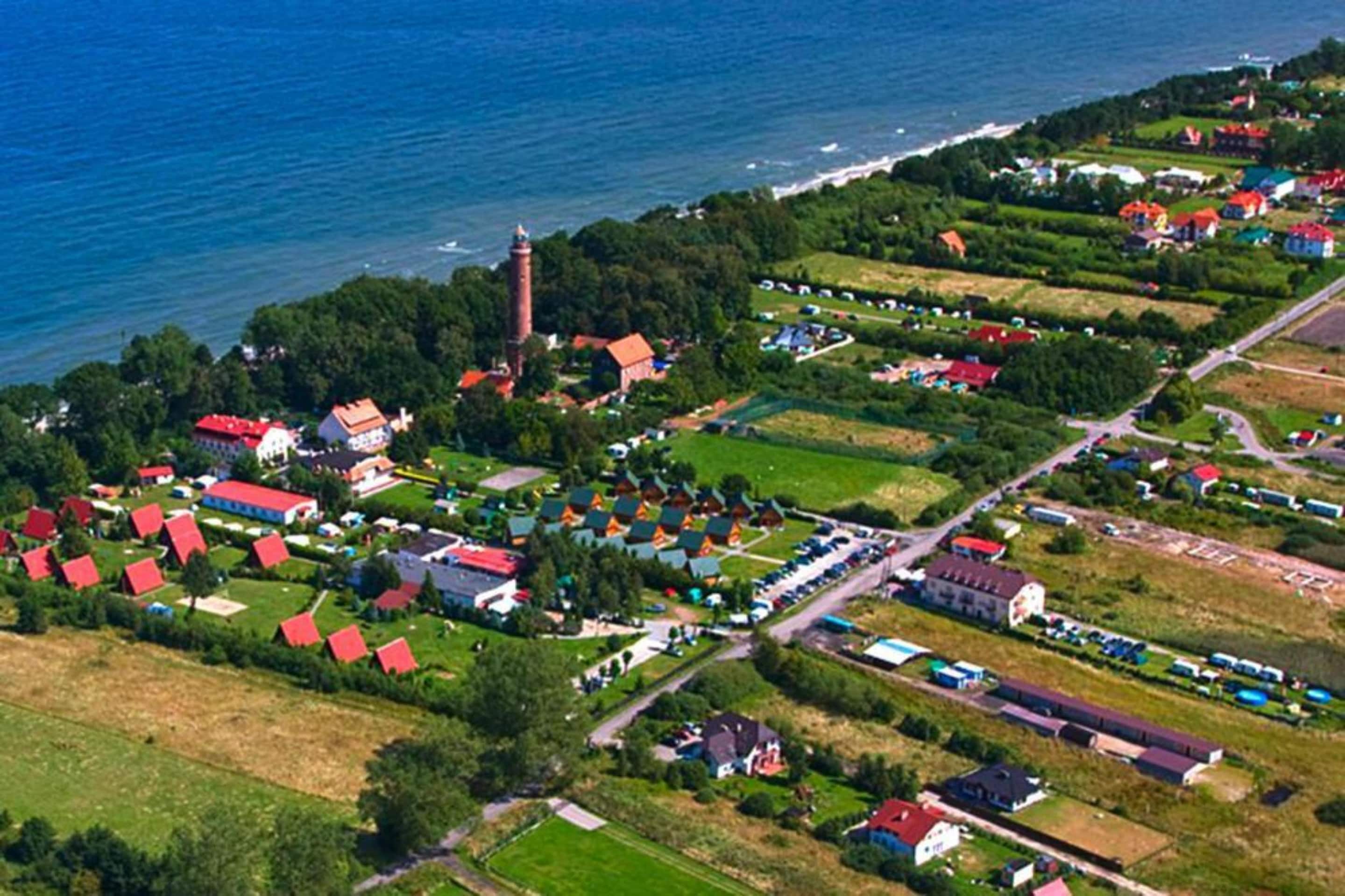 An aerial view of a coastal village with houses, a lighthouse, and a road.