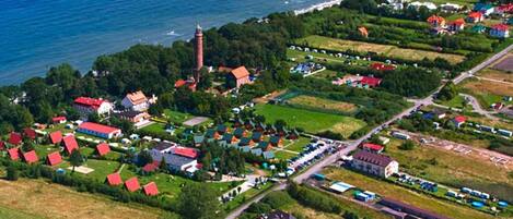 An aerial view of a coastal village with houses, a lighthouse, and a road.