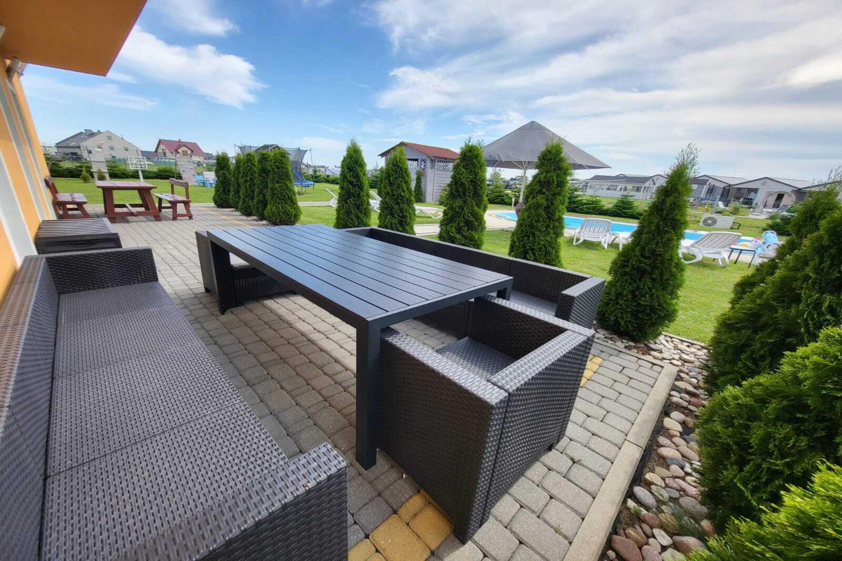 Un patio al aire libre con una mesa y asientos de color oscuro, rodeado de follaje y vistas a una zona residencial.