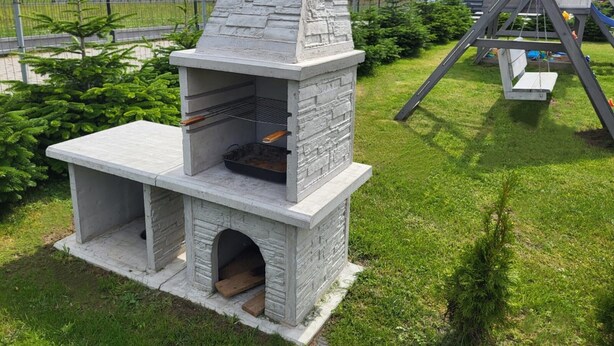 A stone barbecue grill with a chimney, a wooden bench, and a swing set in a grassy area. - Comfortable Premium Class Apartment, Shared Swimming Pool, Gaski (Mielno)