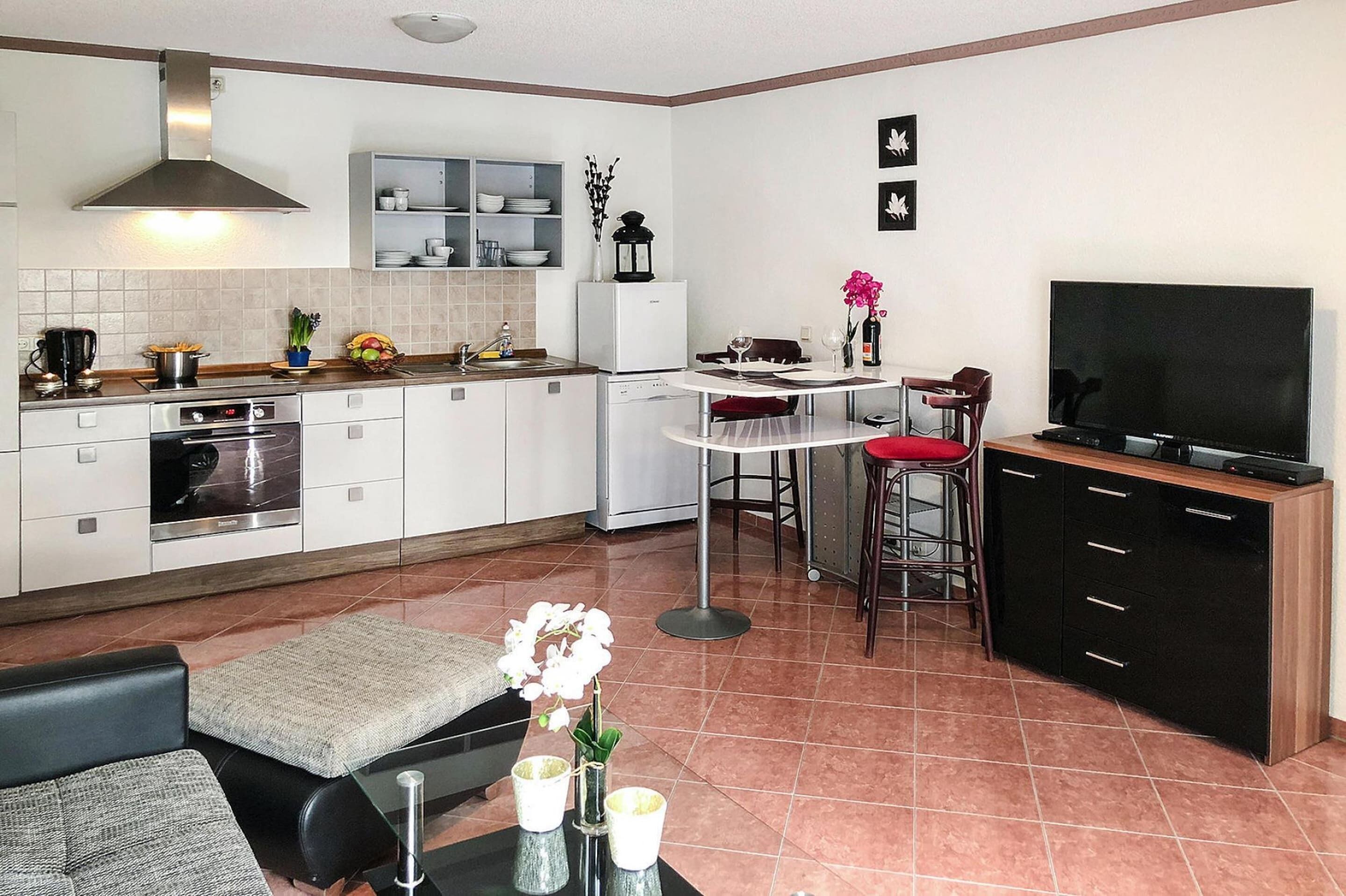 A modern kitchen with white cabinets, a built-in oven, and a dining area with a round table and two bar stools.