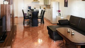 Een moderne keuken met witte kasten, een eettafel met stoelen, een zwarte bank en een televisie op een houten dressoir.