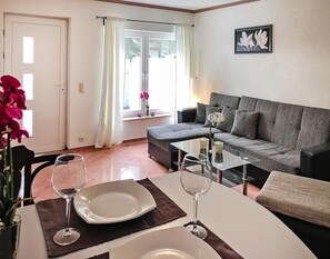 Una sala de estar moderna con un sofá gris, una mesa de centro de vidrio y una mesa de comedor con platos y copas de vino.
