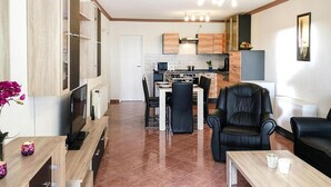 Een moderne woonkamer met een televisie, een eethoek met tafel en stoelen, en een keuken op de achtergrond.