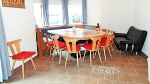 Ein Essbereich mit Holztisch und Stühlen, einer schwarzen Couch und einem Fenster mit Vorhängen.
