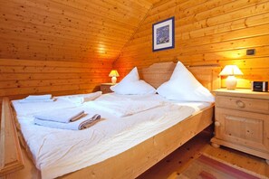 Dormitorio de cabaña de madera con cama, almohadas, mesita de noche y lámpara.