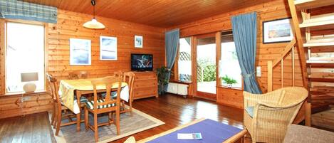 L’intérieur d’un chalet en bois comprend un coin repas, un téléviseur et un escalier.