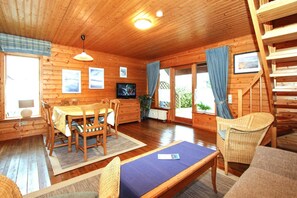 Interior de una cabaña de madera con comedor, televisor y escalera.