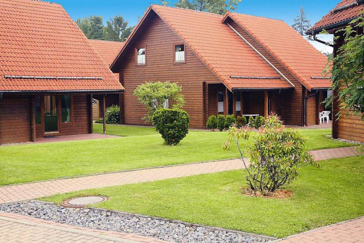 A row of wooden cabins with red-tiled roofs, a paved pathway, and well-maintained lawns.