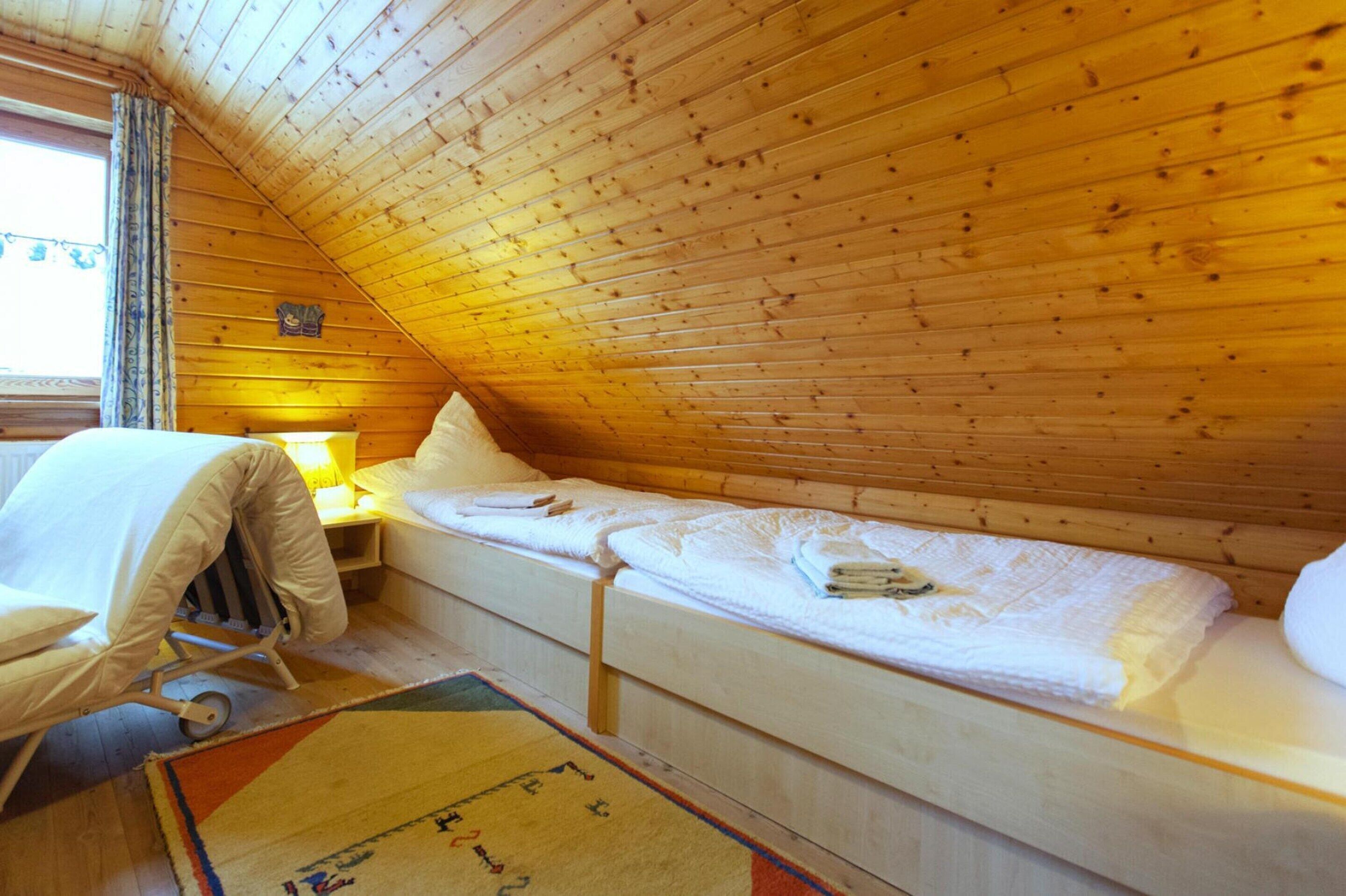 A small, cozy room with a wooden ceiling, a single bed, a nightstand, a lamp, and a stroller.