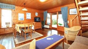 L’intérieur d’un chalet en bois comprend un coin repas, un téléviseur et un escalier.
