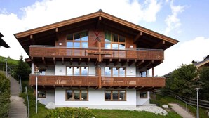 A two-story wooden chalet with a balcony on the upper floor, set on a hillside with a staircase leading up to it. - Holiday Flat Barlerhof Xxl, Konigsleiten (Wald im Pinzgau)