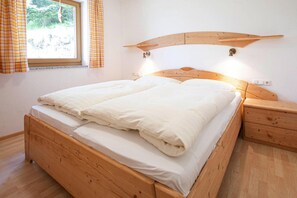 A wooden bed with a headboard, a bedside table, and a window with curtains. - Holiday Flat Barlerhof Xxl, Konigsleiten (Wald im Pinzgau)