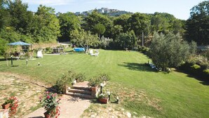 Une pelouse bien entretenue, agrémentée d’une terrasse, de mobilier d’extérieur et offrant une vue sur une colline parsemée de bâtiments.