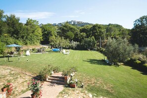 A well-maintained lawn with a patio area, outdoor furniture, and a view of a hill with buildings. - Apartment in Chiusdino (Siena)