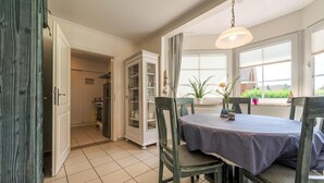 A dining area with a table set for two, surrounded by chairs, and a cabinet with glass doors. - Apartment in Friedrichskoog-spitze With Parking Space (Friedrichskoog)
