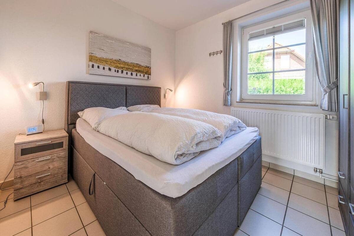 A bedroom with a bed, bedside table, lamp, and a window with curtains.