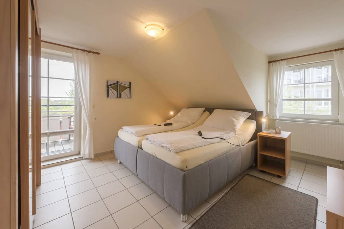 A bedroom with a bed, a nightstand, a window, and a view of the outside.