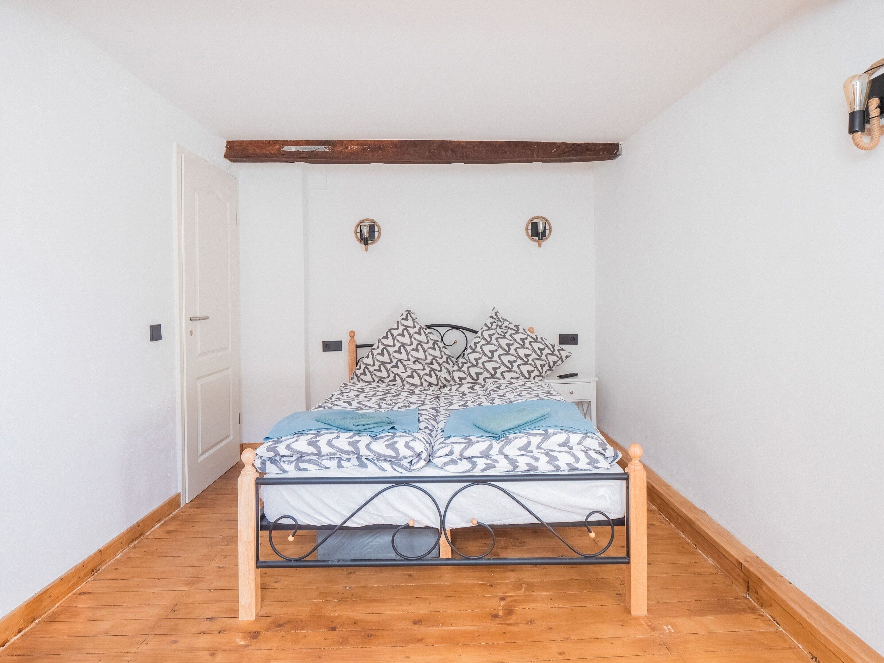 Quarto com estrutura de cama de madeira, roupa de cama estampada e porta branca.