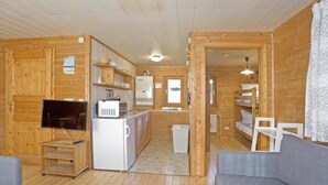 A wooden cabin interior with a living area, kitchenette, and a bedroom with a bunk bed. - Ferienhaus in Hechthausen mit Terrasse (Hechthausen)