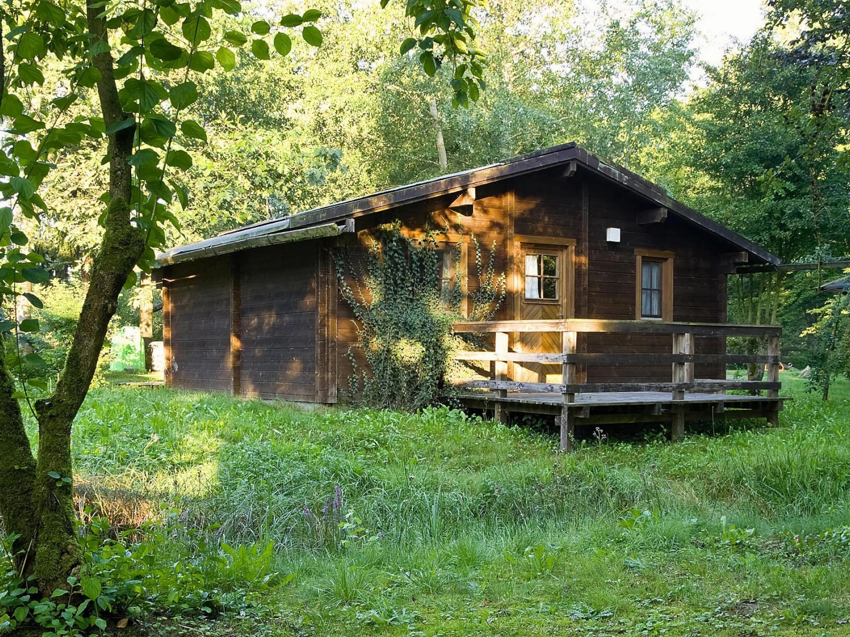 A rustic cabin with a wooden deck, surrounded by lush greenery.