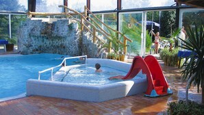 An indoor swimming pool with a slide, stone walls, and a wooden staircase. - Ferienhaus in Hechthausen mit Terrasse (Hechthausen)