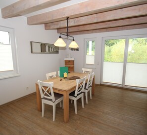 Un área de comedor con una mesa y sillas de madera, una lámpara colgante, una ventana con persianas y un espejo en la pared.