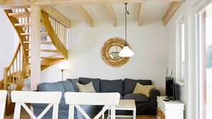 A modern living room with a staircase, a grey sofa, white furniture, and a TV on a white cabinet. - Ferienhaeuser im Ferienpark, Hechthausen (Hechthausen)