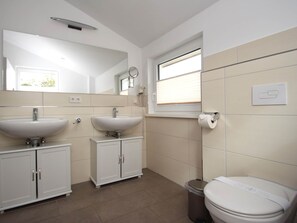 Un baño moderno con dos lavamanos, un inodoro y un ventanal con persianas.