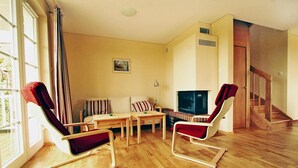 Ein geräumiges Wohnzimmer mit Holzboden, einer Couch, zwei Schaukelstühlen, einem kleinen Tisch und einem Fernseher.