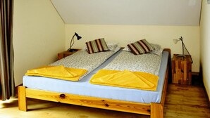 Ein Doppelbett mit zwei Kissen und einer gelben Decke, Nachttische aus Holz und ein Holzboden.