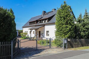 A two-story house with a dark roof, white walls, and a gated driveway.