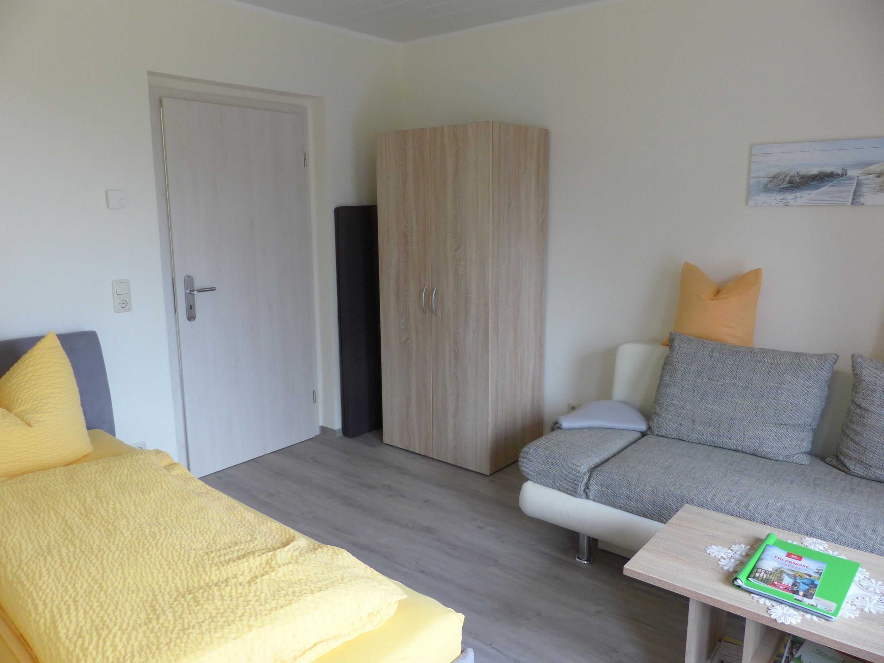 Et værelse med en seng, en sofa, et skab og et lille bord med en bog.