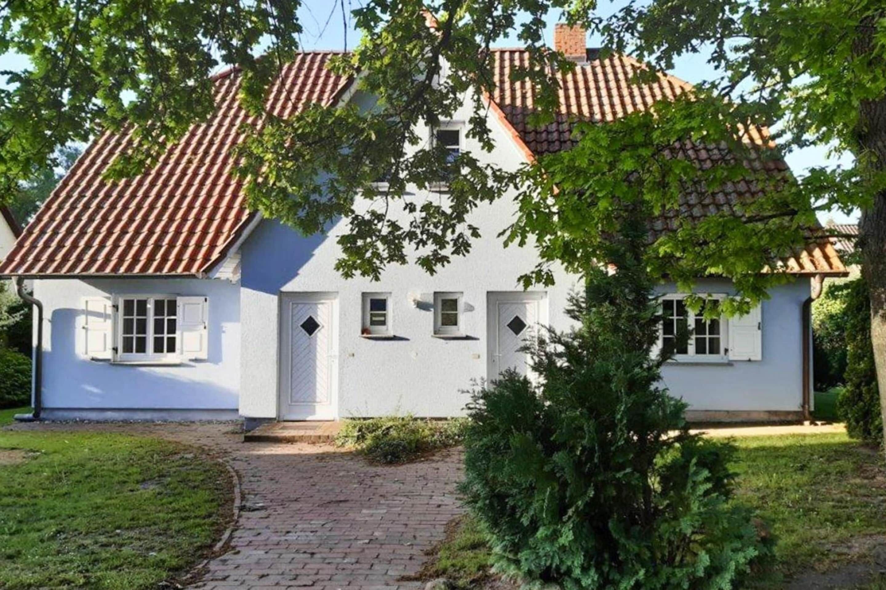 A white house with a tiled roof, a brick pathway leading to the entrance, and a small garden area.