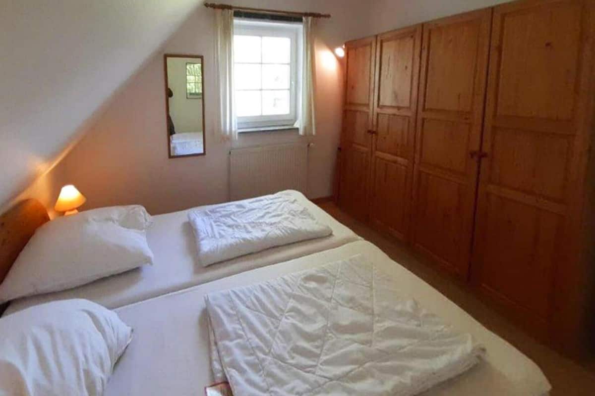 A bedroom with two beds, a window, wooden wardrobe, and a mirror.