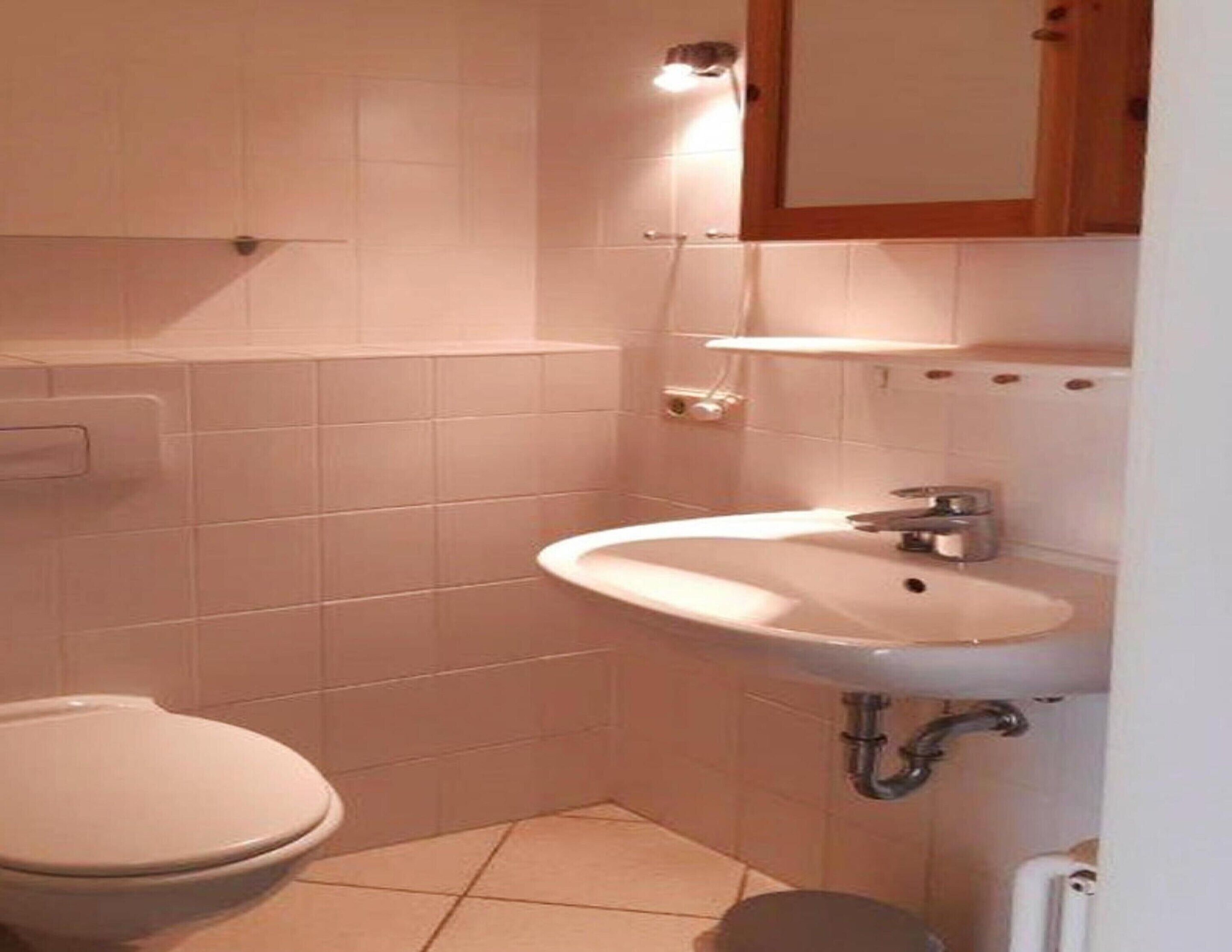 Een kleine, schone badkamer met witte tegels, een toilet, een wastafel en een spiegel.
