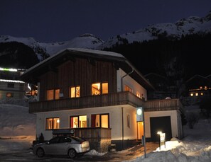 A two-story wooden cabin with a car parked in front, surrounded by snow-covered mountains. - Apartment in Steeg in a Beautiful Setting (Steeg)