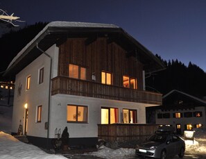 A two-story wooden building with a balcony, a car parked in front, and snow on the ground.
