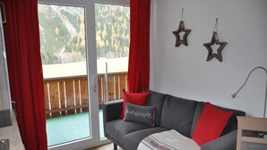 A living room with a grey sofa, red and white cushions, a blanket, and two star decorations on the wall. - Apartment in Steeg in a Beautiful Setting (Steeg)