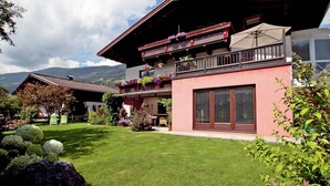 Una chalet a due piani con un balcone, un giardino e uno sfondo montuoso.