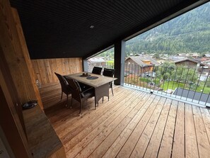 A wooden deck with a table and chairs, overlooking a residential area with houses and a mountain in the background. - Apartment in Bramberg am Wildkogel With Balcony (Bramberg am Wildkogel)