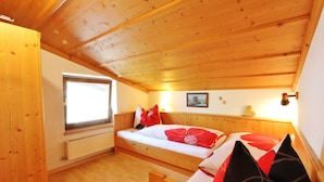 Una camera in legno con un letto, una finestra, un termosifone e un soffitto in legno.