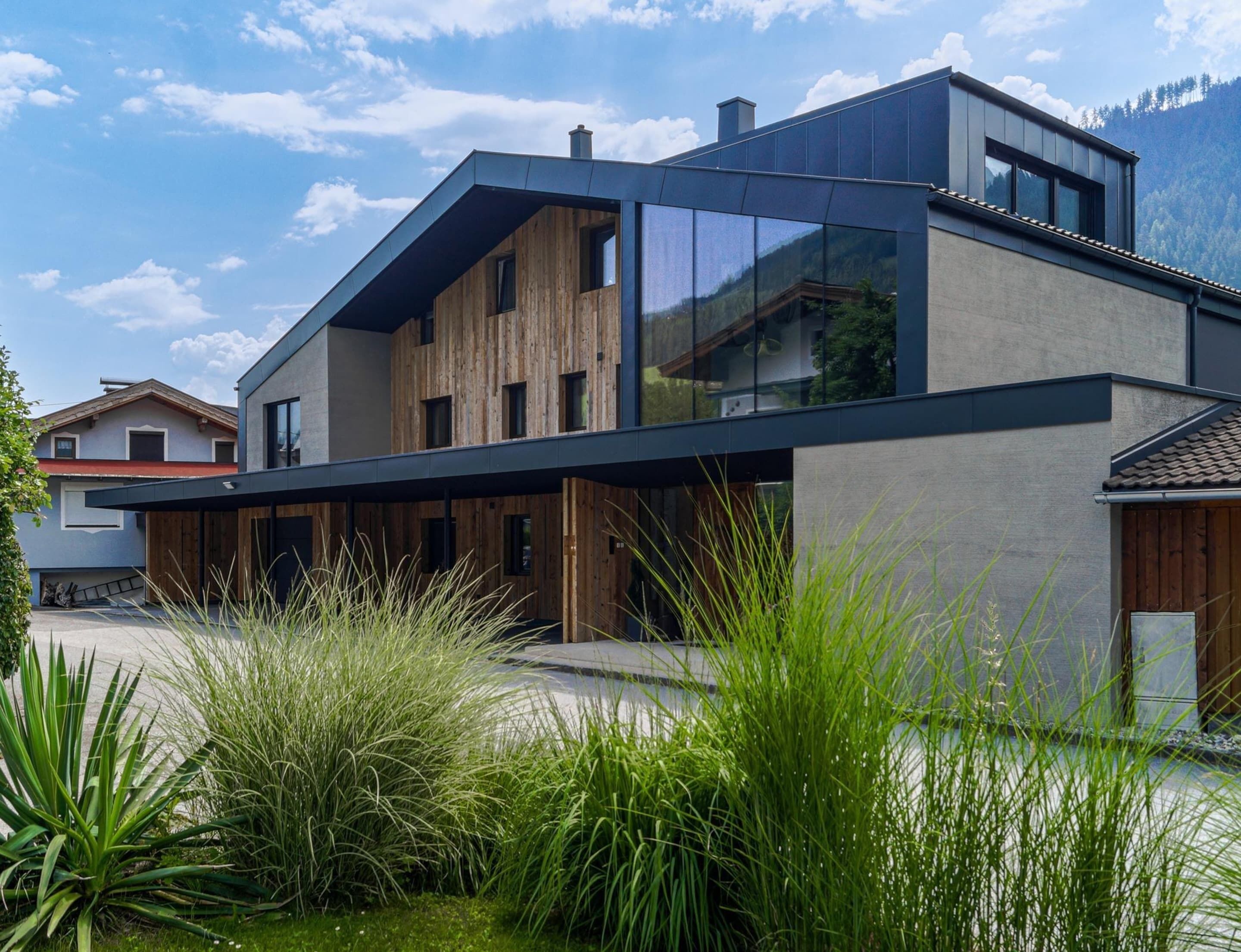 Una casa moderna de dos pisos con techo plano, ventanas amplias y fachada de madera.